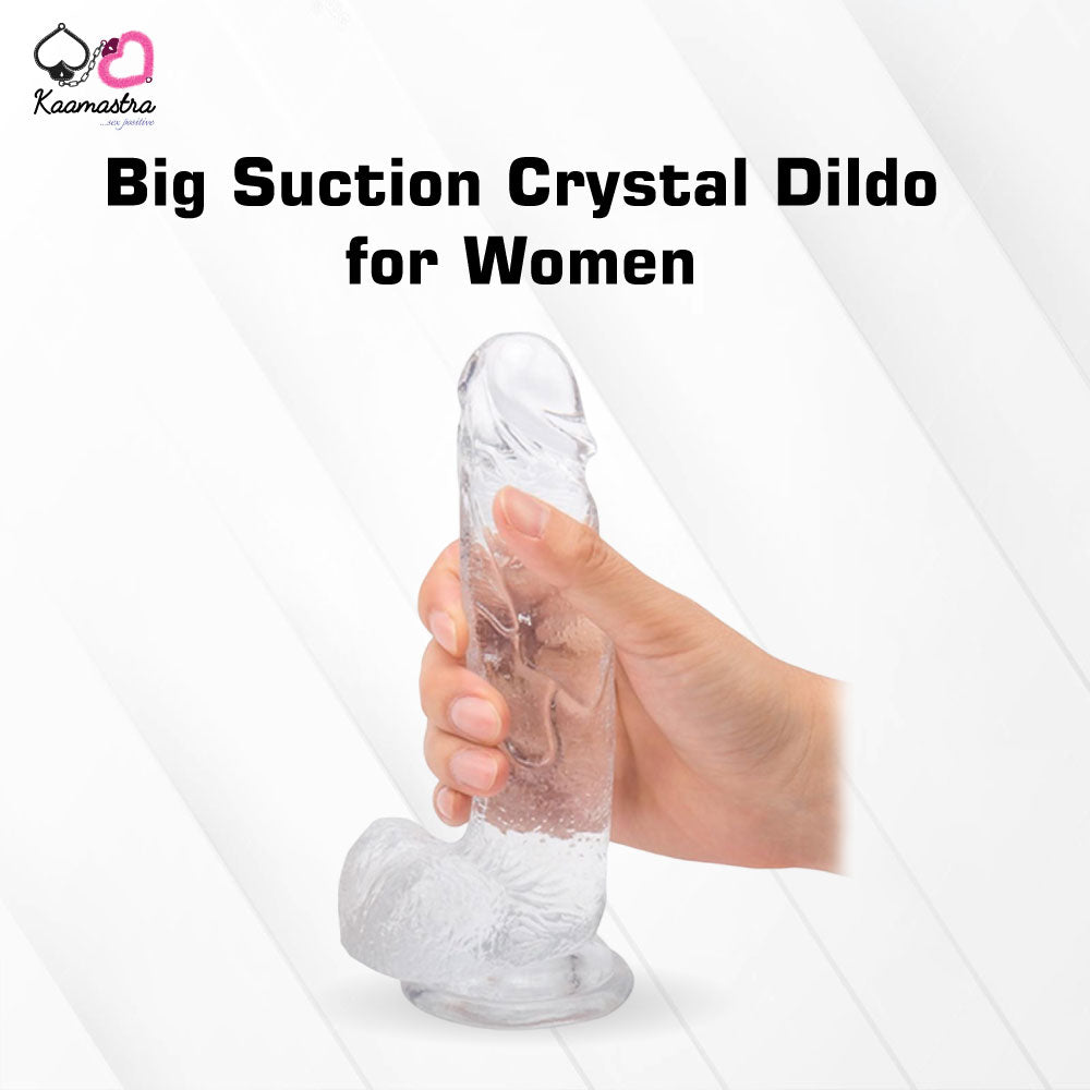 Clear suction crystal dildo held by a hand on a white background with 'Kaamastra' branding.