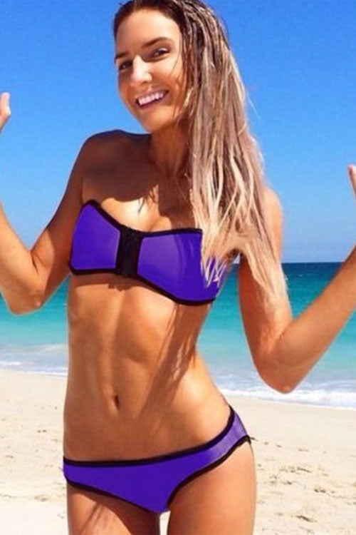 A woman at the beach wearing a purple strapless bikini with a steel ring for support.
