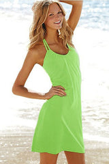 A woman standing on a beach wearing a blue mini summer beach dress with spaghetti straps.