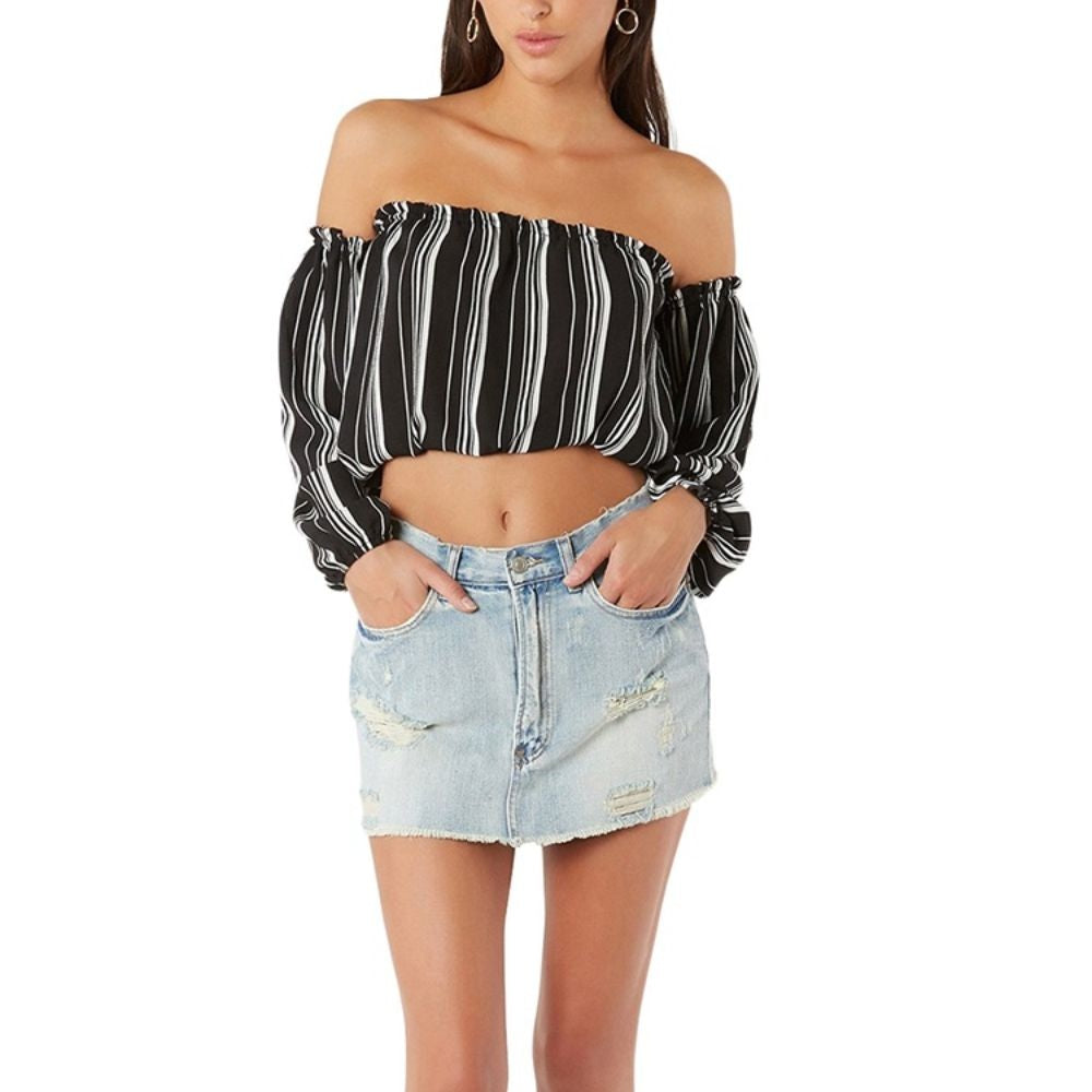 A woman wearing a black and white striped strapless crop top with long sleeves, paired with a denim skirt.