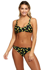This image features a model showcasing a reversible bikini swimsuit with a vibrant pineapple print. The swimsuit includes a swim top with crisscross straps and removable bra paddings, paired with a matching low waist bottom that also exhibits crisscross detailing on its sides.