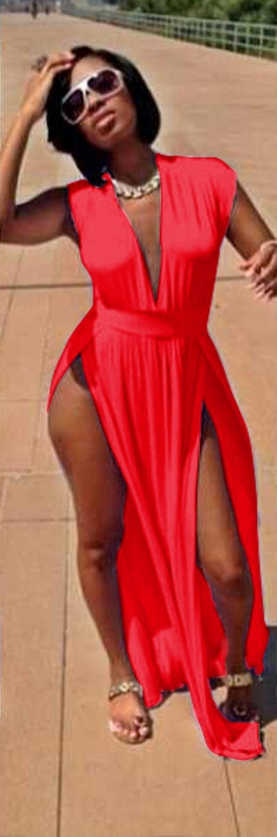 A woman wearing a red, V-neck, sleeveless, maxi dress with side slits, posing on a pathway.