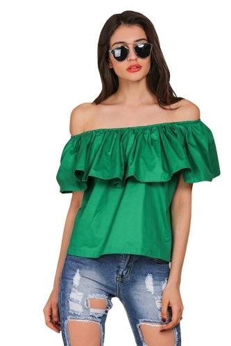 A woman wearing a green off the shoulder ruffles crop top with sunglasses on and denim shorts.